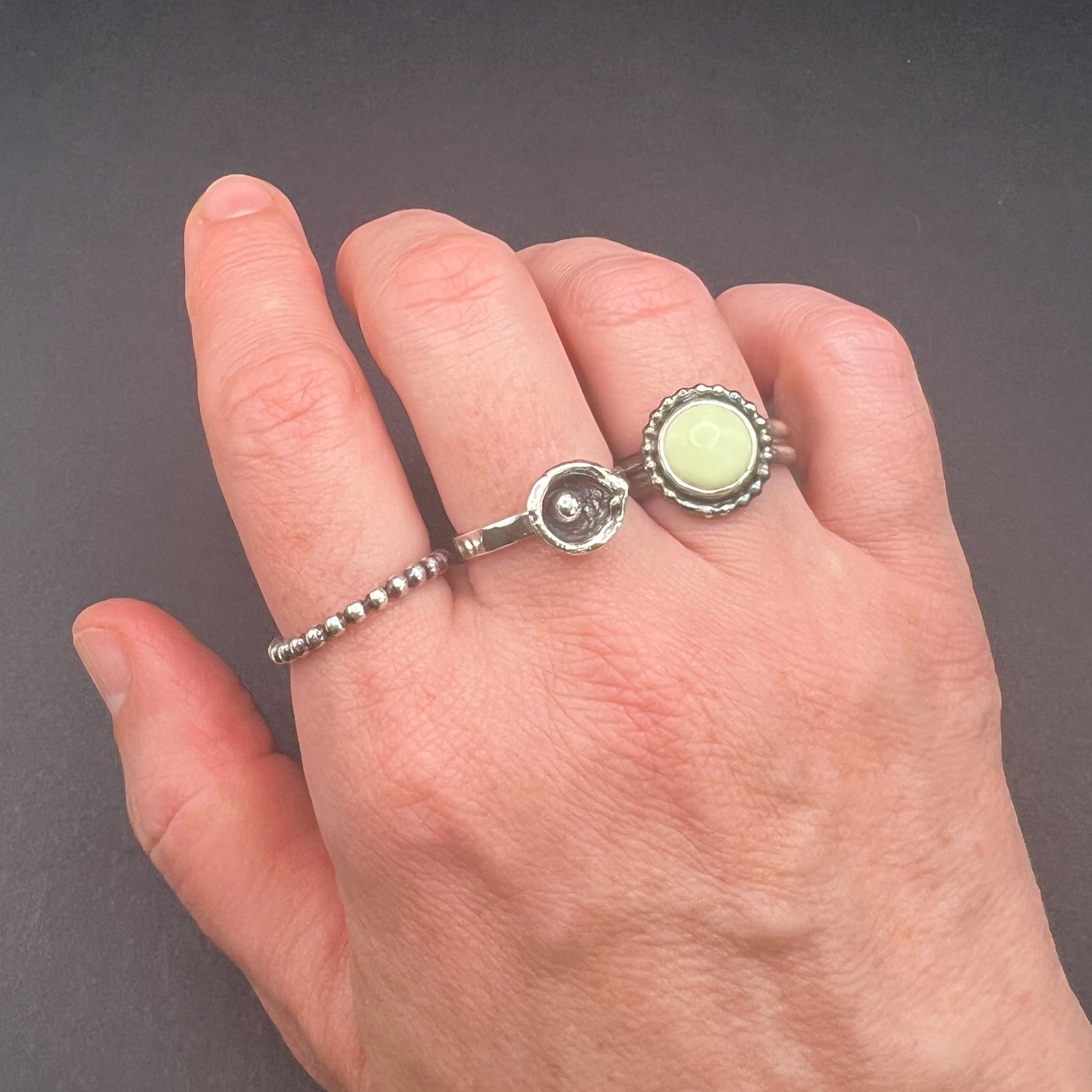 Hand wearing 3 different rings.  One bead wire ring, one water cast ring and one lemon chrysoprase feature ring.  